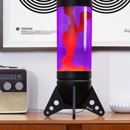 Originali Mathmos Rokit raketos formos lavos lempa – Juoda / Violetinė / Raudona Didelė juoda Mathmos Rokit raketos formos lavos lempa su violetiniu skysčiu ir raudona lava retro stiliaus interjere ant medinės spintelės